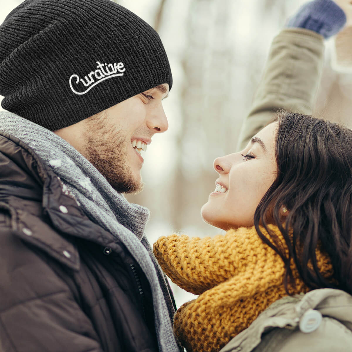 Couple embrace outdoors, man wearing black Curative Printing beanie.