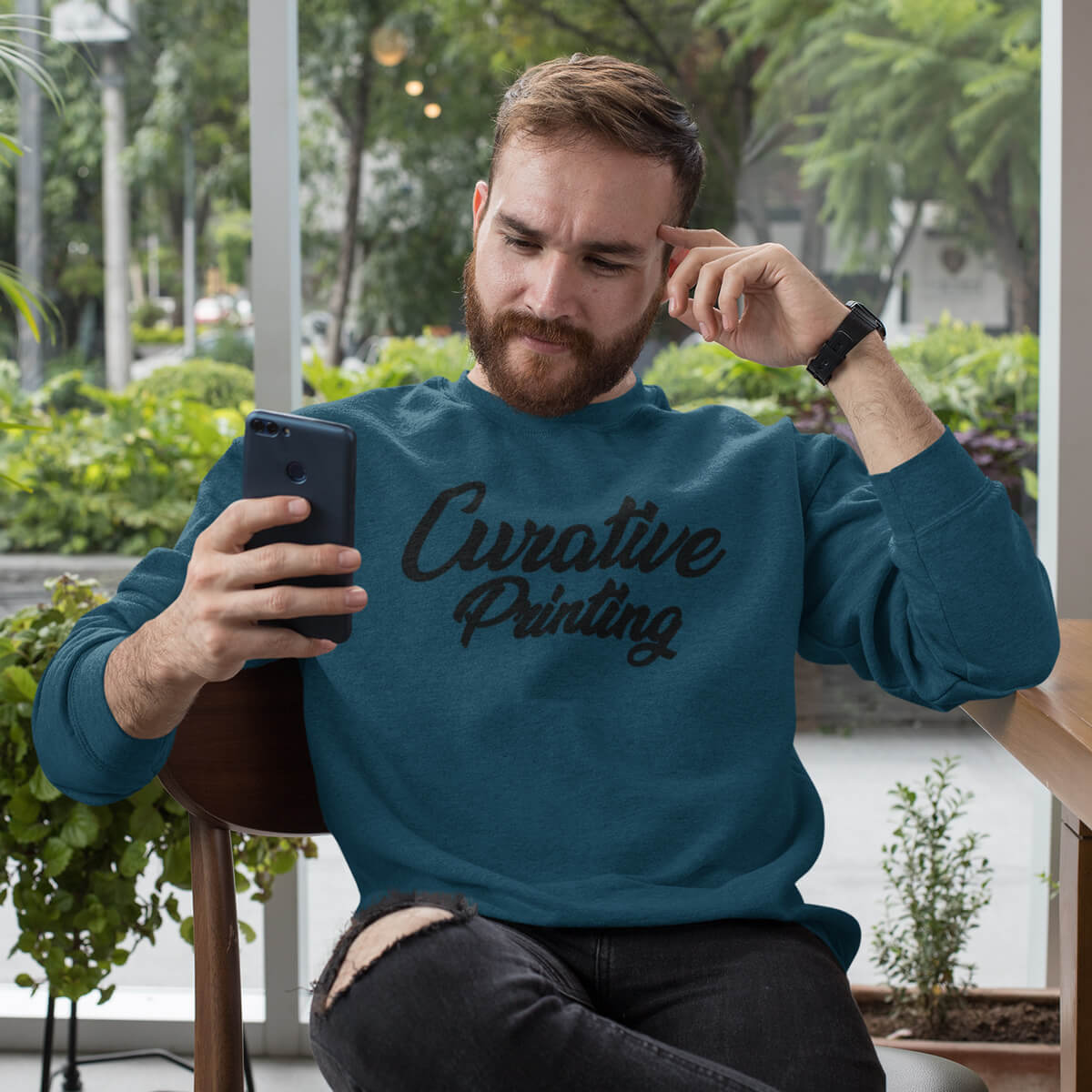Lounging man wearing Curative Printing crewneck sweatshirt