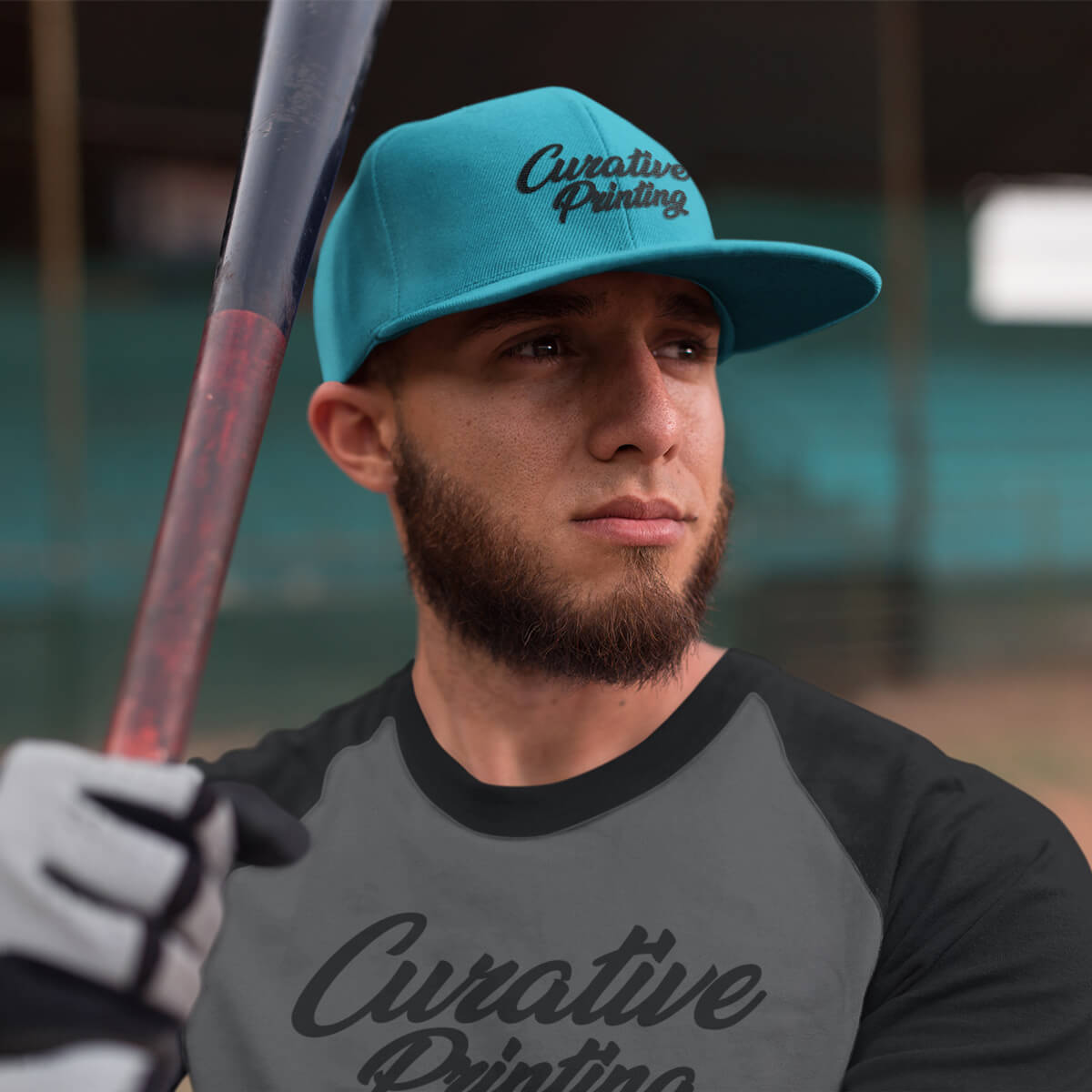 Man holding baseball bat wearing turquoise ball cap with black curative printing logo imprint