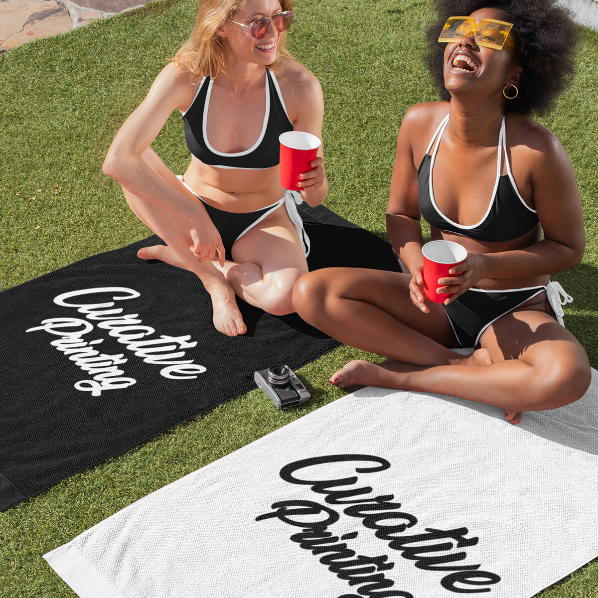 Happy women sunbathing on black and white colored beach towels promotional towels by curative printing