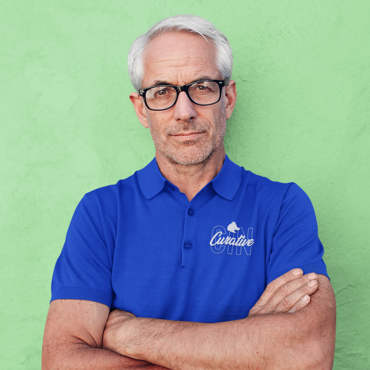 Man leans against textured wall wearing a blue polo collar shirt with white curative printing logo imprint