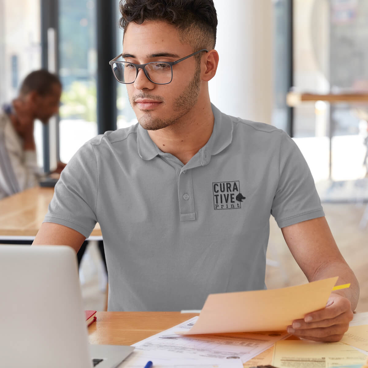Man works in a cafe wearing a grey polo collar shirt with black curative printing logo imprint