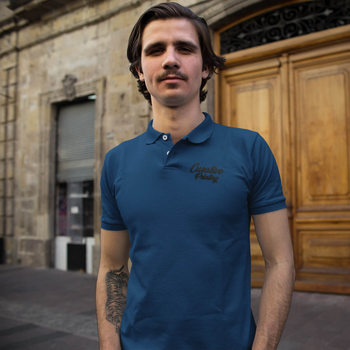 Man stands in the street wearing a blue polo collar shirt with black curative printing logo imprint