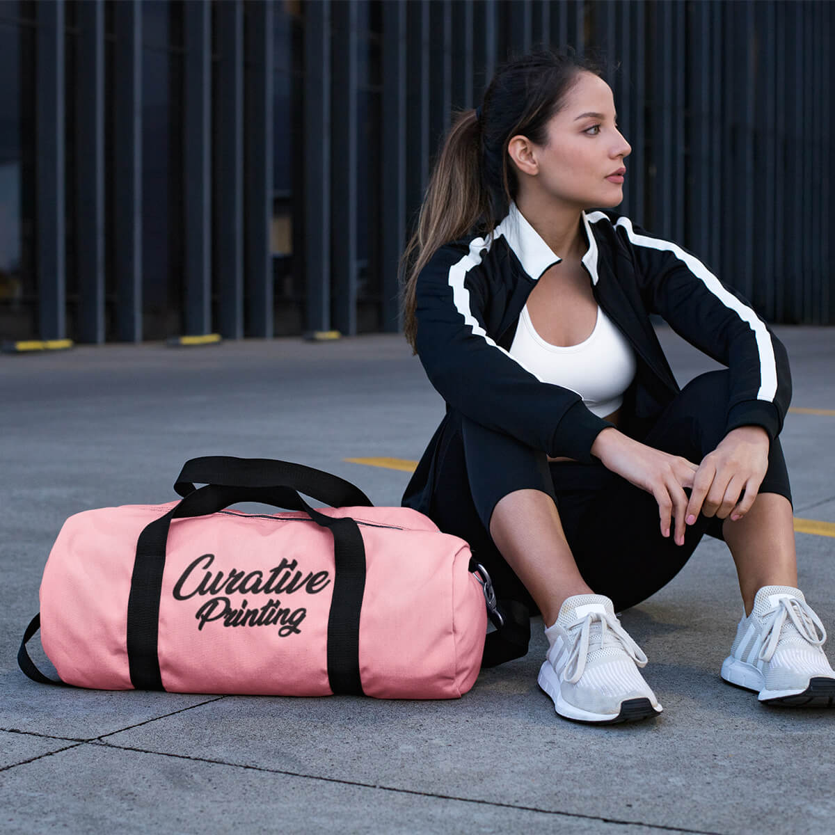 Sporty woman sitting by pink custom promotional duffle bags by curative printing