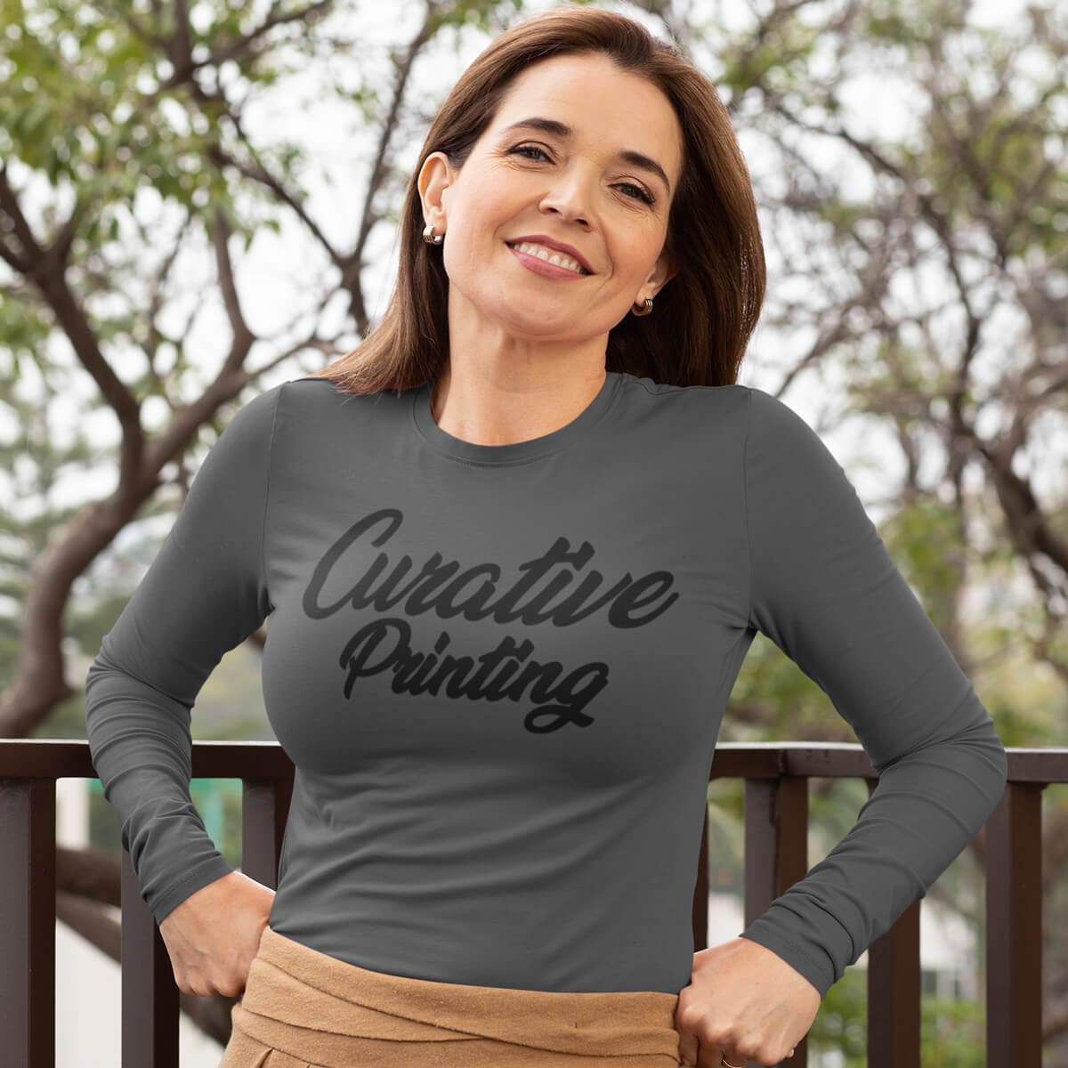 Happy woman standing outside wearing a grey long sleeve t-shirt tee with black curative printing logo imprint
