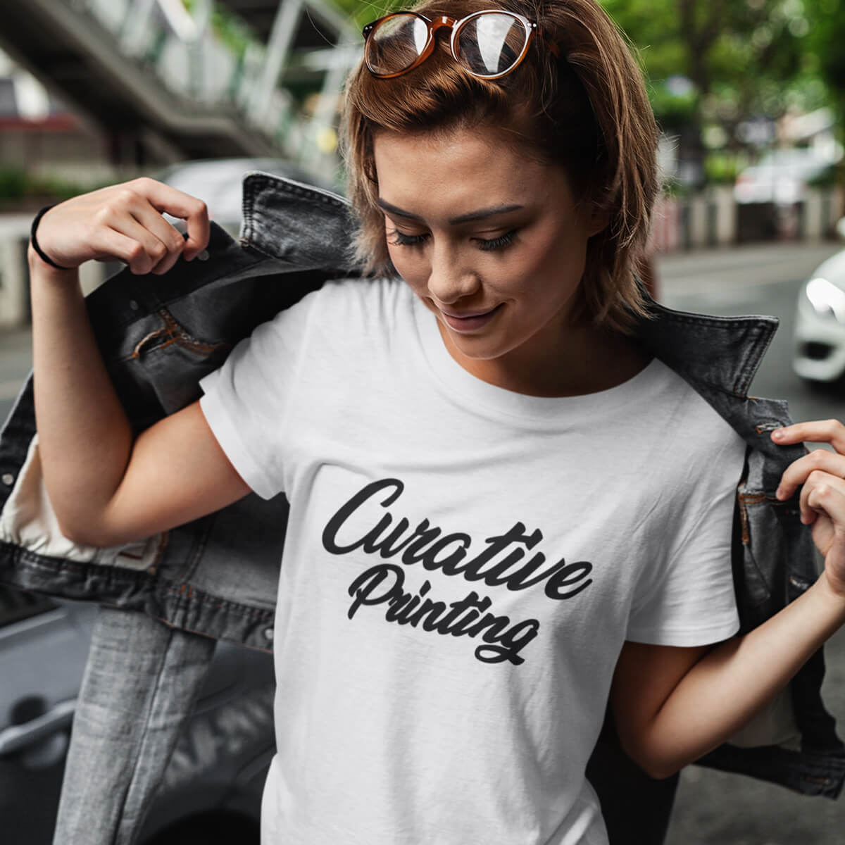 Trendy woman outside pulling on jacket wears white short sleeve t-shirt tee with black curative printing logo imprint