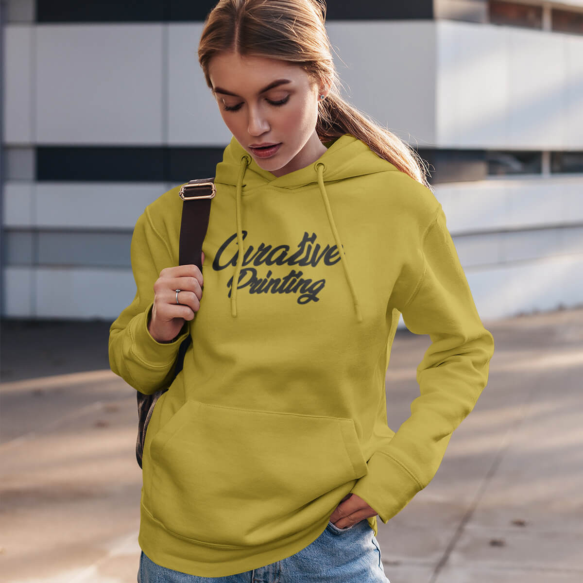 Woman with a bag wearing a yellow pullover hoodie sweatshirt with black curative printing logo imprint